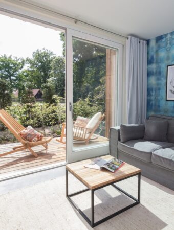 Blick aus dem Wohnbereich im Familienhotel Niedersachsen auf die Terrasse mit zwei Schaukelstühlen aus Holz
