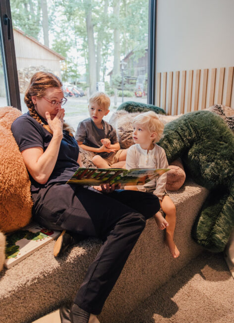 Kinderbetreuerin liest in einer Kuschelecke Kindern ein Buch vor