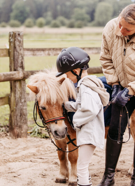 Junge streichelt ein Pony mit der Reitlehrerin.