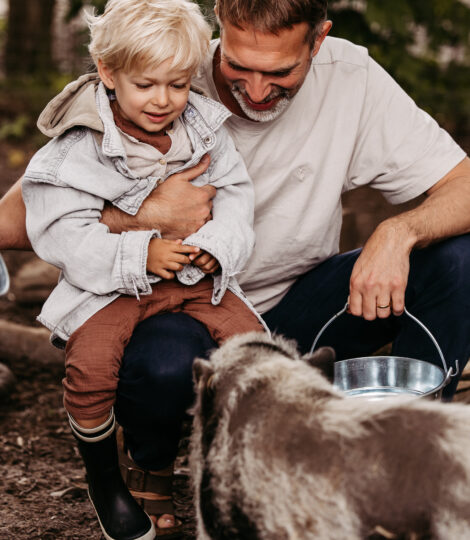 Vater mit Sohn auf dem Schoss beim Schweine füttern.