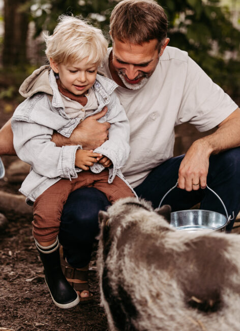 Vater mit Sohn auf dem Schoss beim Schweine füttern.