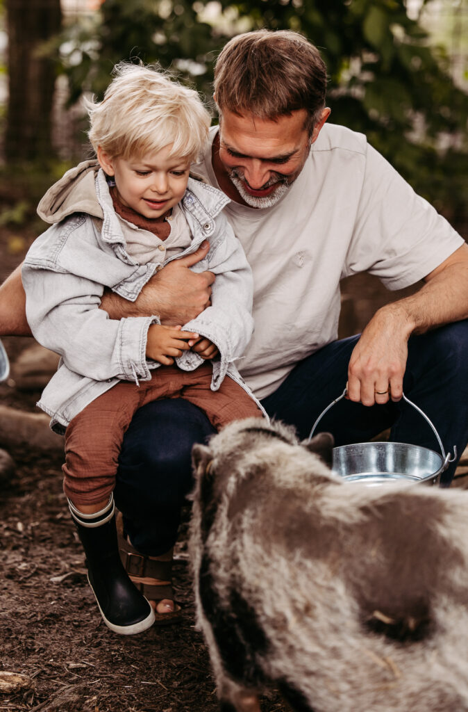 Vater mit Sohn auf dem Schoss beim Schweine füttern.